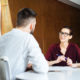 Smiling beautiful businesswoman in glasses talking to young businessman in meeting room
